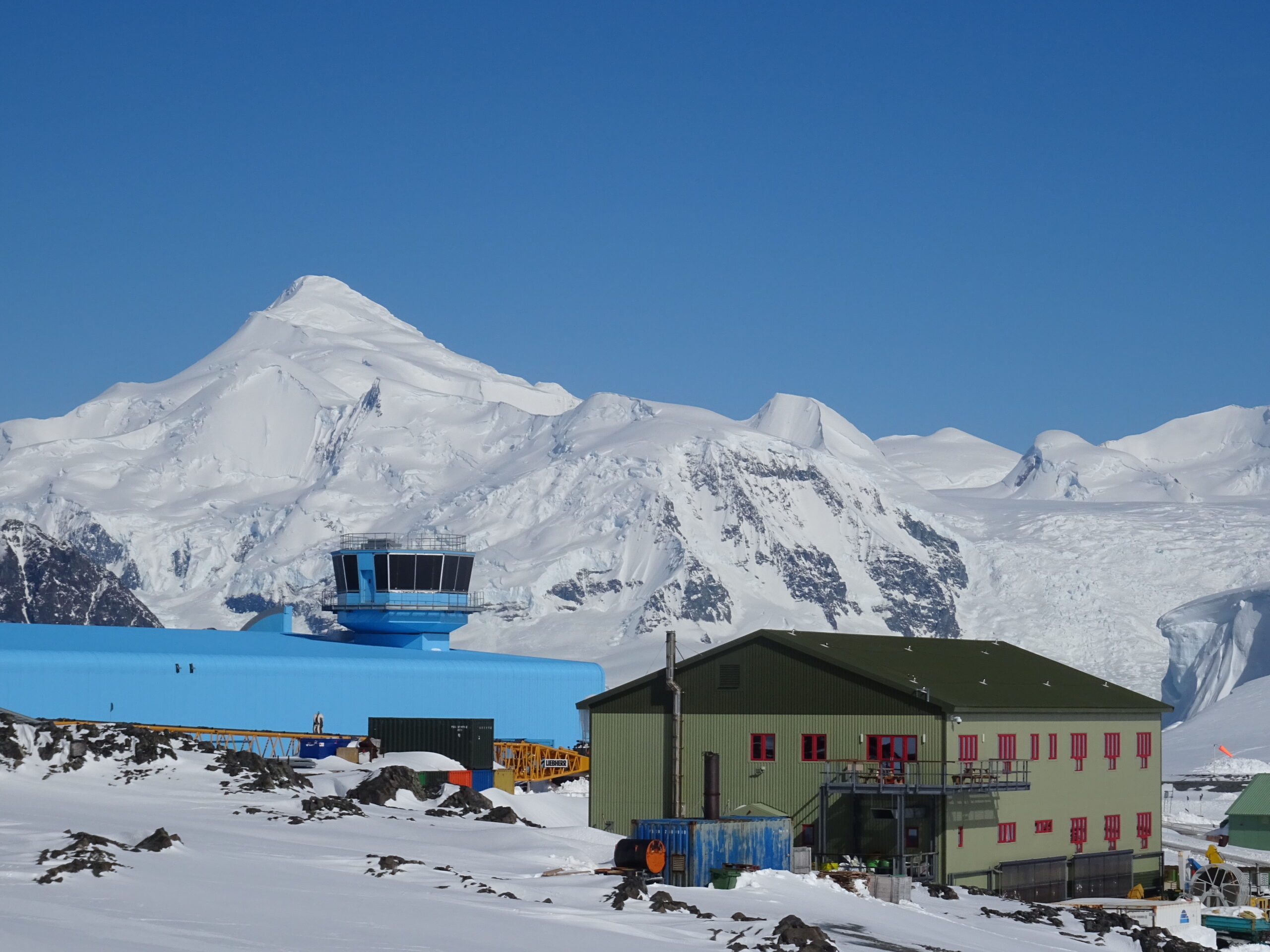 A snow covered mountain with a large blue building and a large green building in front of it.