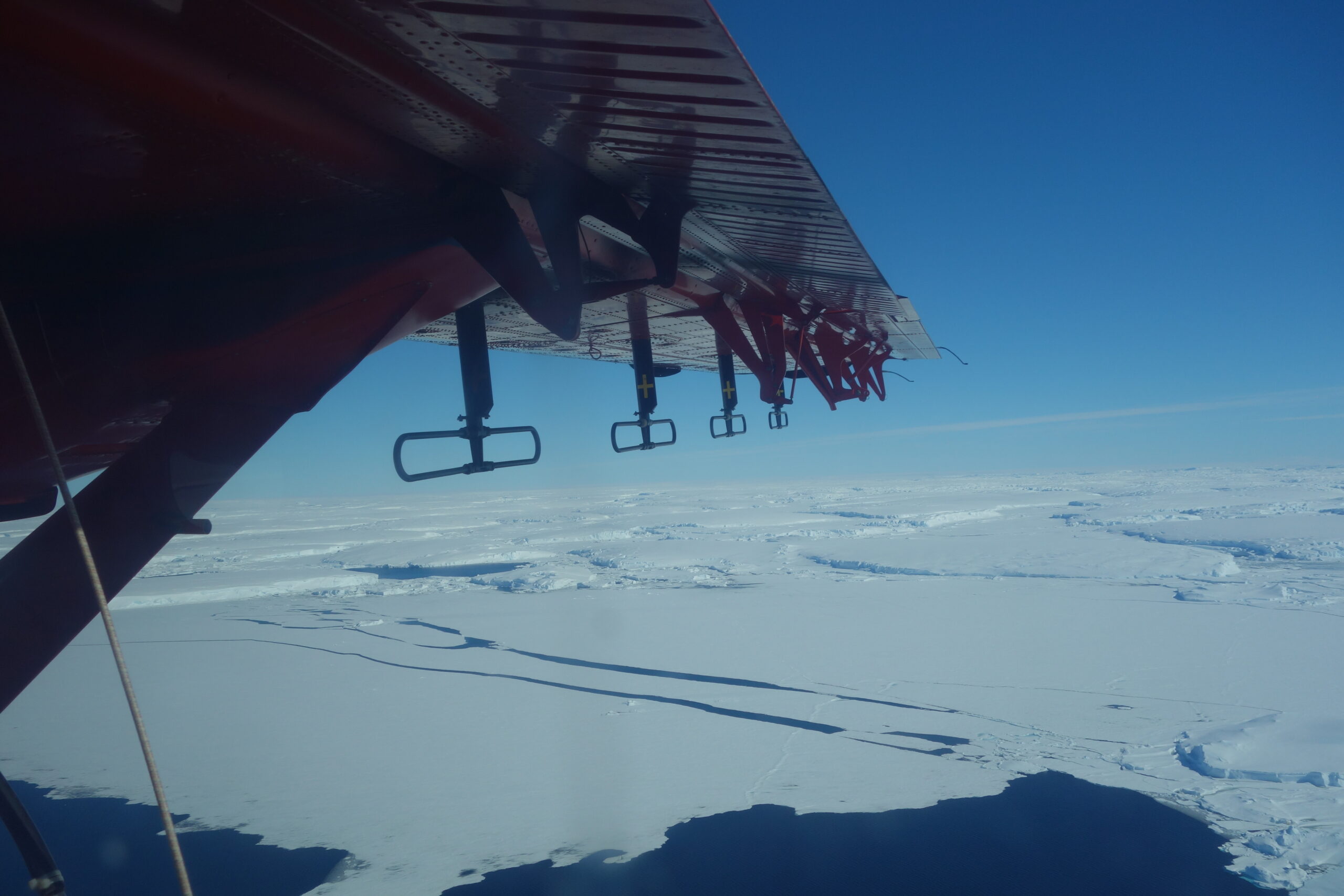 A view out of a plane window of a red plane wing and a vast ice sheet below