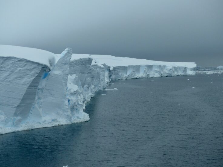 The edge of a glacier with grey sky above and grey-blue ocean below