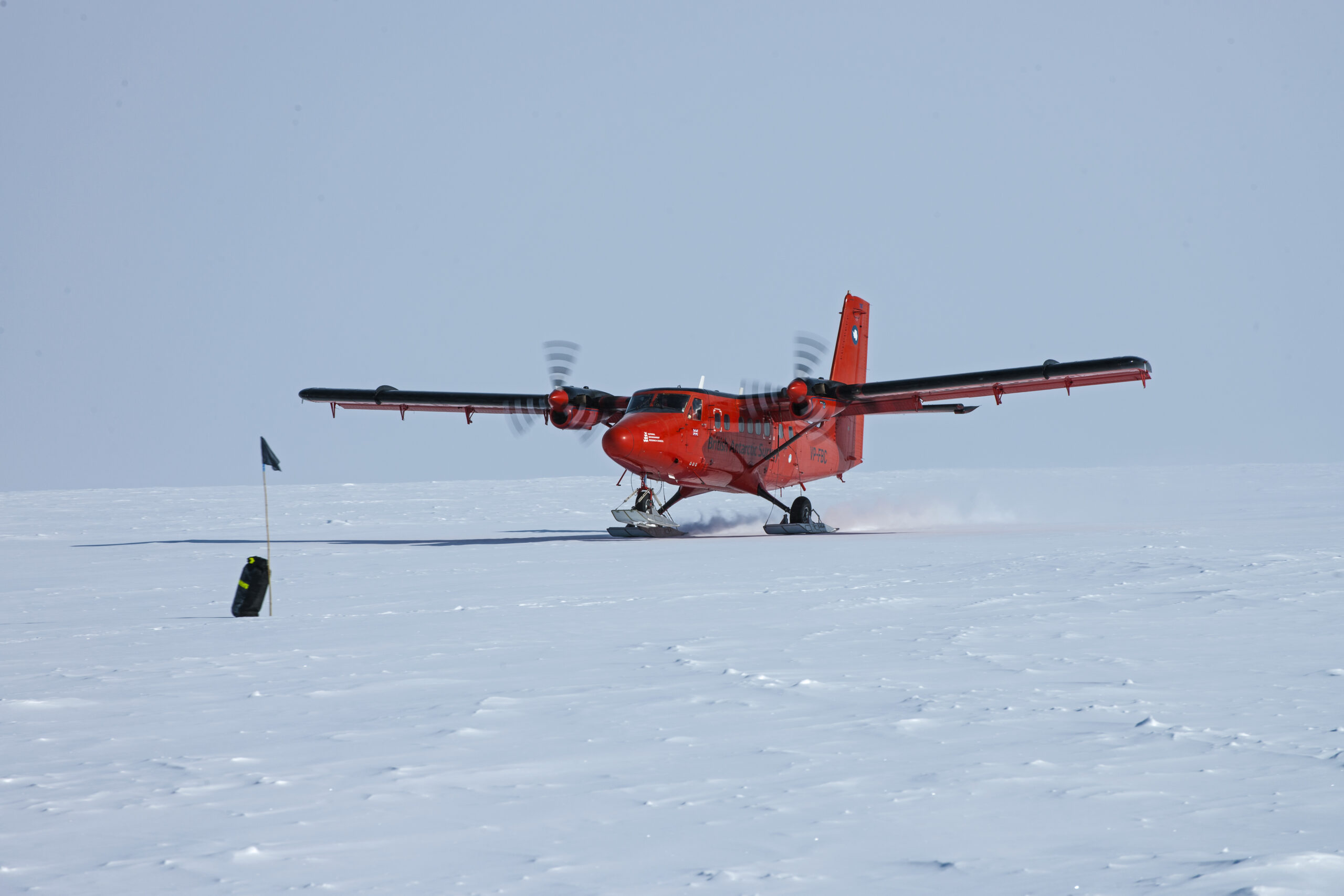 An orange aircraft, with skis instead of wheels, landing on the white, icy Antarctic continent