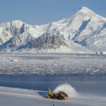 A digger on snow with a snowy mountain in the background