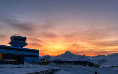 A sunset over the snow with a blue building on the left