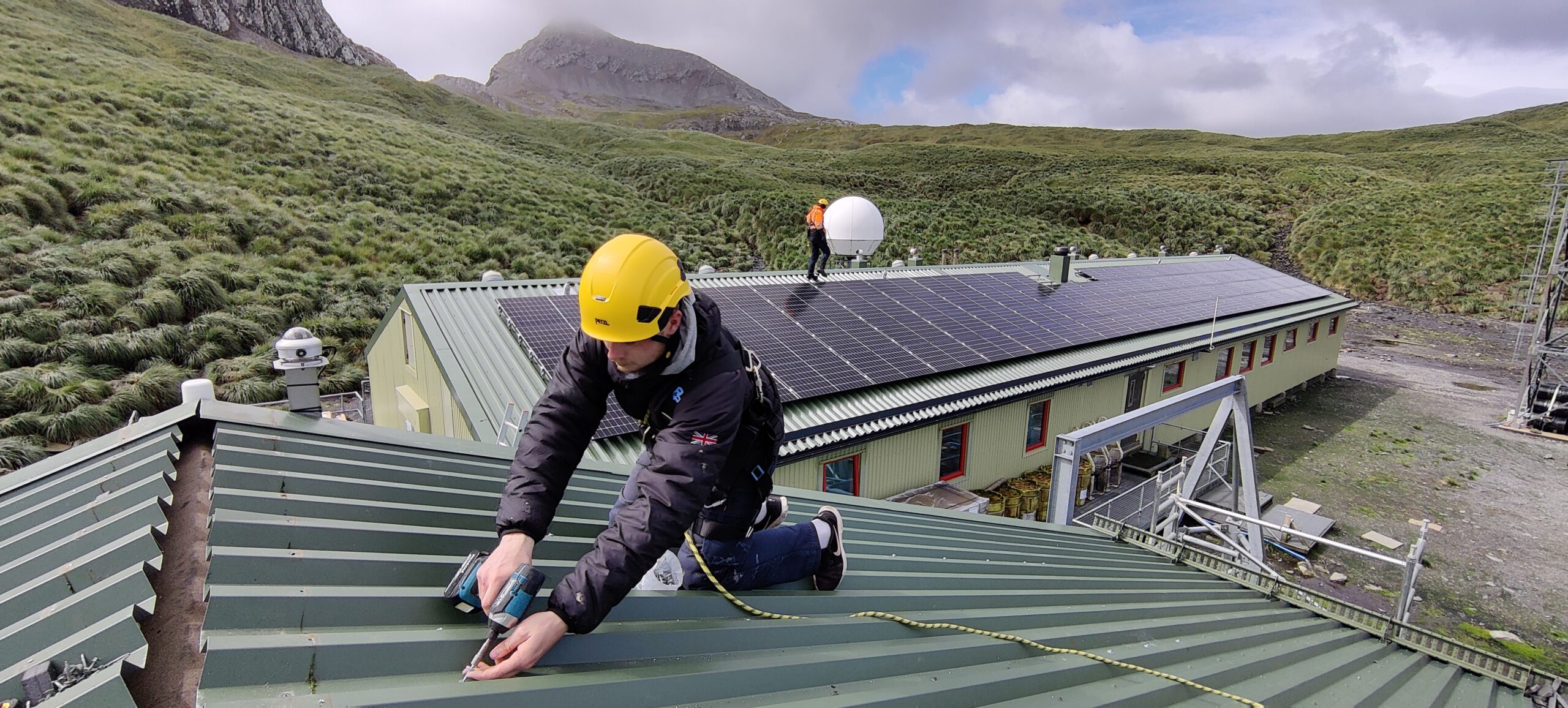 A man working on top of the roof of a building with mountains behind him.