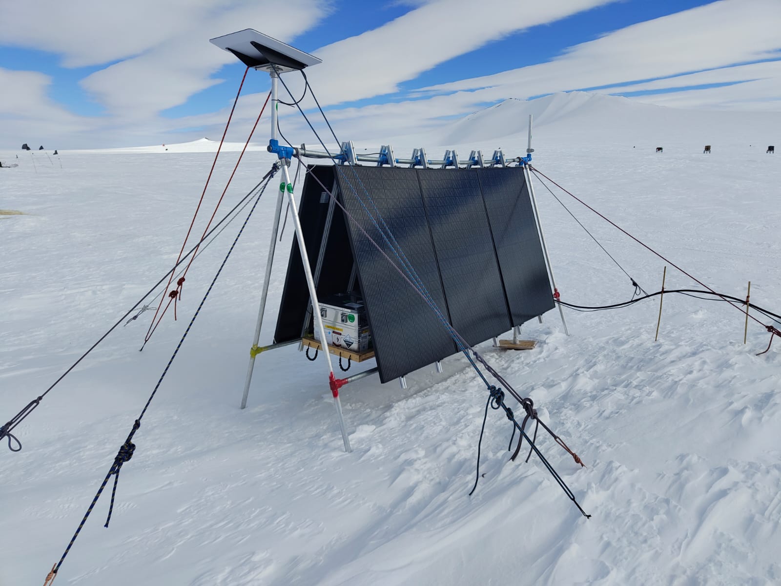 A snow covered landscape with an A frame and cables on the ice.